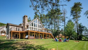 Uma casa grande com varanda coberta, chaminé de pedra e um quintal gramado com área de estar externa.