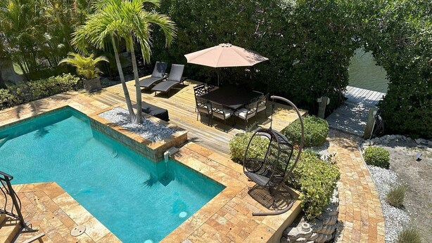 Una piscina con muelle de madera, sillones de descanso y zona de estar cubierta.