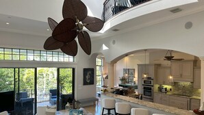 Amplia sala de estar con un gran ventilador de techo, cocina con electrodomésticos modernos y un balcón con mobiliario para exterior.