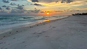 Una playa con atardecer, orilla arenosa y edificios a lo lejos.