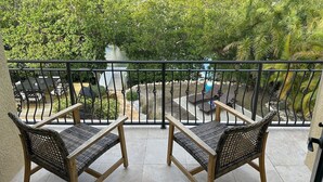 Un balcón con sillones de mimbre y vistas a un jardín exuberante y palmeras.