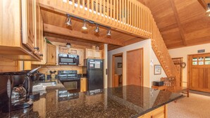 A kitchen with granite countertops, wooden cabinets, a microwave, a refrigerator, and a coffee maker. - Spacious Cedar Chalet w/ Hot Tub & Pool Table (Swanton)