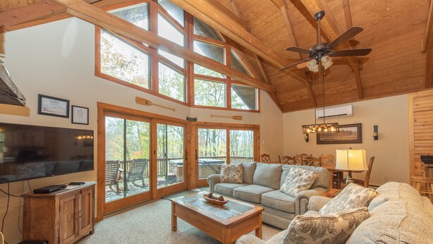 A spacious living room with a large television, wooden ceiling, and a ceiling fan. - Spacious Cedar Chalet w/ Hot Tub & Pool Table (Swanton)