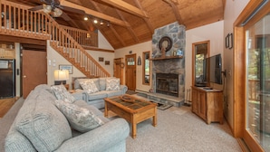 A spacious living room with a high ceiling, wooden staircase, and a stone fireplace. - Spacious Cedar Chalet w/ Hot Tub & Pool Table (Swanton)