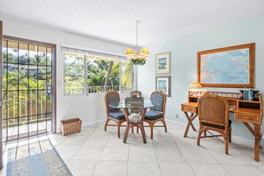 A dining area with a glass table, wicker chairs, a map on the wall, and a view of palm trees through the window. - LAST MINUTE DISCOUNT SPECIAL!  New Ductless Split A/C System! (Kailua-Kona)