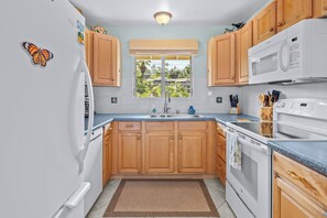 Une cuisine avec des meubles en bois, un four à micro-ondes, une cuisinière et une fenêtre donnant sur un paysage verdoyant.