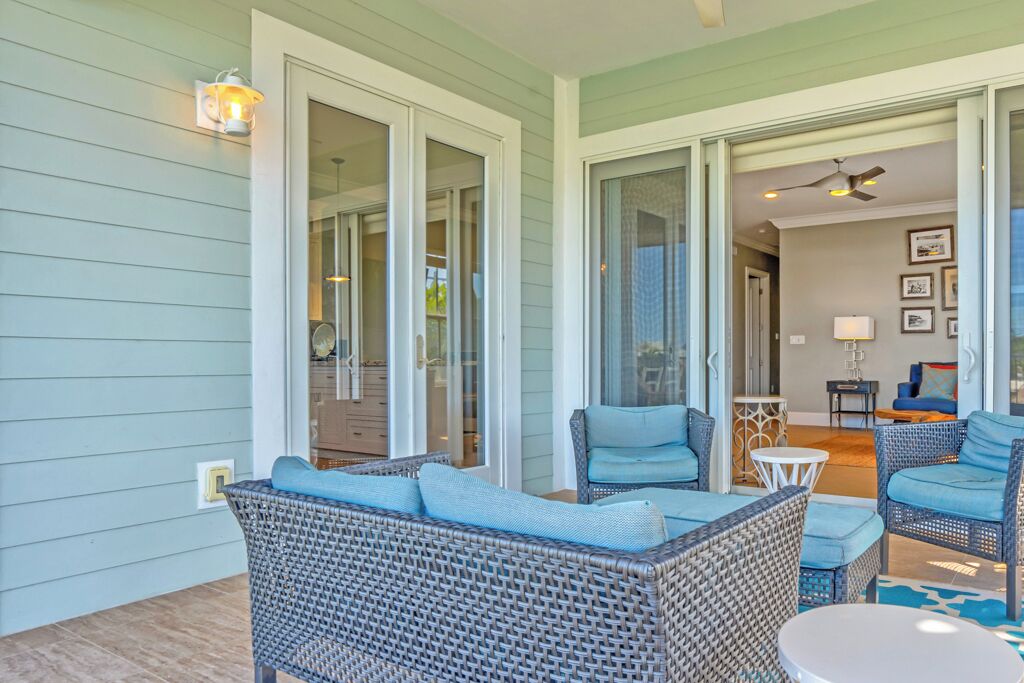 Un patio techado con mobiliario de mimbre, puertas de vidrio que dan a una habitación y un ventilador de techo.