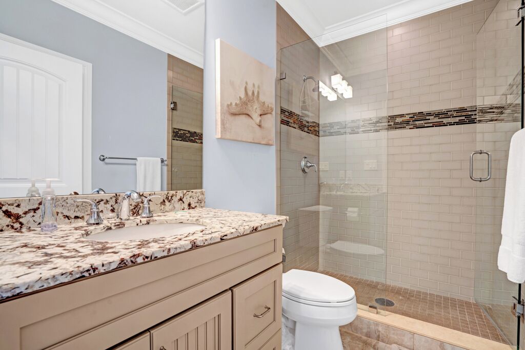 A bathroom with a marble countertop, a white toilet, a glass shower enclosure, and a towel rack.