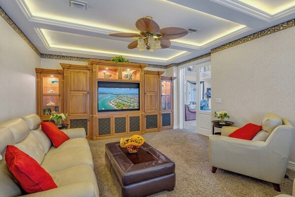 A living room with a large flat-screen TV, leather sofas, a coffee table, and a ceiling fan. - P05 - 5 bedroom Ocean Front home with Private pool and deep water dockage. (Key Colony Beach)