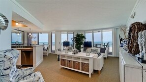 A spacious living room with a view of the ocean, a white sofa, a coffee table, and a dining area with chairs.