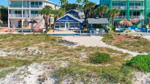 A beachfront hotel with multiple buildings, including a prominent blue structure with a pool and lounge area. - Reef at The Arbors—Charming 50s Cottage Steps from Beach w/ Pool & Lush Grounds (Indian Rocks Beach)