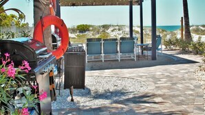 A covered outdoor seating area with a grill, lounge chairs, and a lifebuoy. - Reef at The Arbors—Charming 50s Cottage Steps from Beach w/ Pool & Lush Grounds (Indian Rocks Beach)