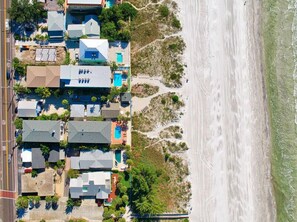 An aerial view of a coastal residential area with houses, some with swimming pools, and a beach in the background. - Reef at The Arbors—Charming 50s Cottage Steps from Beach w/ Pool & Lush Grounds (Indian Rocks Beach)