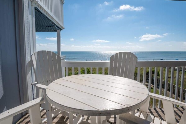 Een wit houten terras met een ronde tafel en twee stoelen, met uitzicht op een strand.
