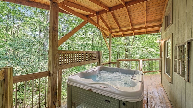 Un bain à remous en bois installé sur une terrasse, avec vue sur une forêt.