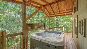 A wooden hot tub on a deck with a view of a forest.