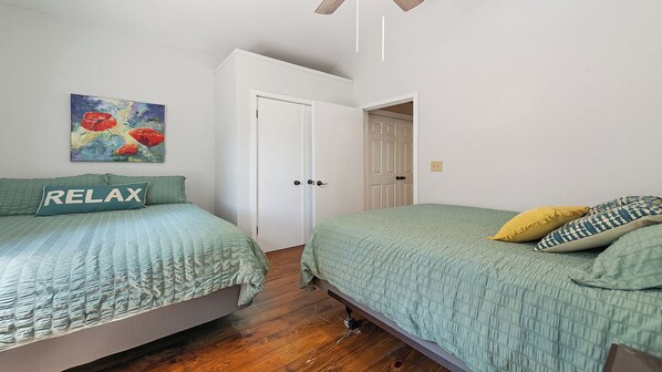 A bedroom with two beds, a painting on the wall, and a door leading to another room.