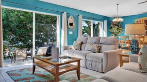 A living room with a sofa, coffee table, and a view of greenery outside.