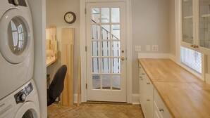 A laundry room with a washing machine, a chair, a door with a window, and a wooden cabinet. - Congress Garden Suite- Off Street Parking Included! (Savannah)
