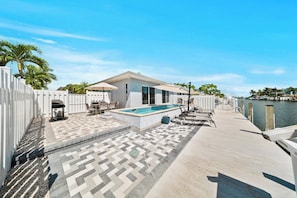 A pool area with a patio, lounge chairs, and a view of the water.