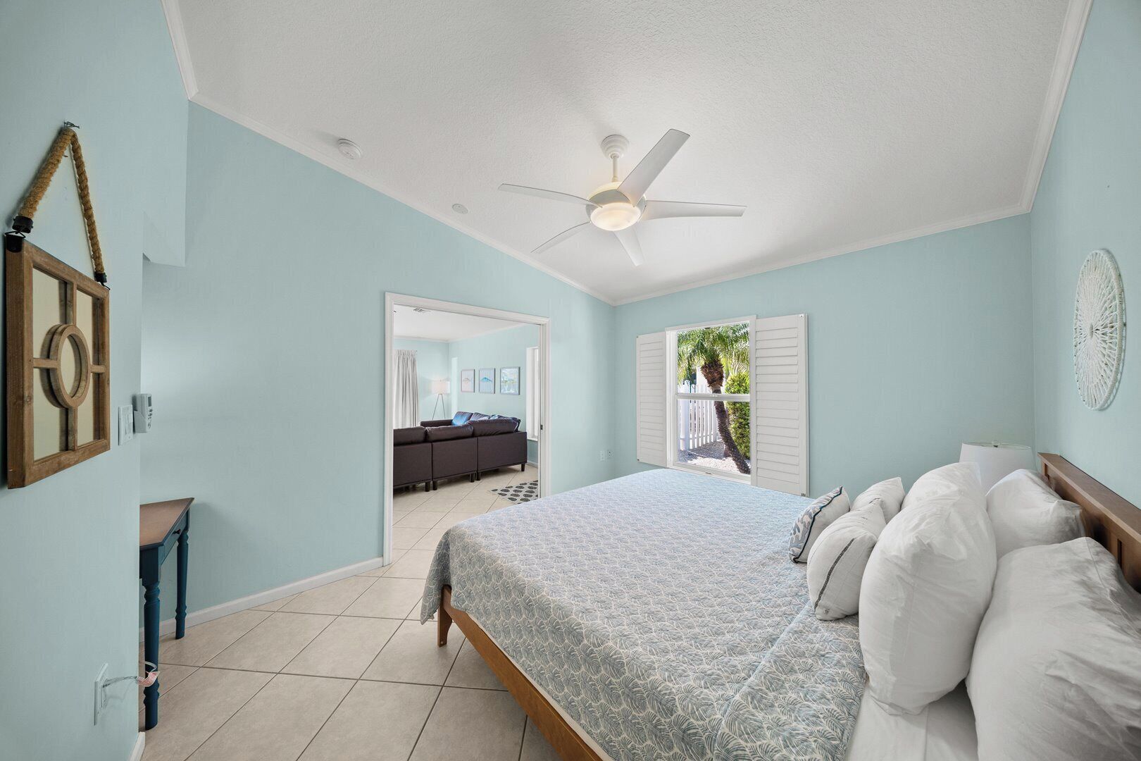 A bedroom with a bed, a ceiling fan, a view of a living area, and a door leading outside.
