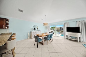 A modern living room with a dining area, a TV, and a view of a pool.