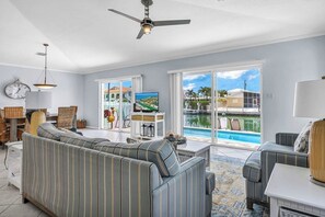 Un salón con sofá, televisor y vista a una piscina.