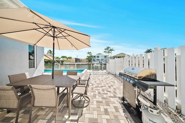 An outdoor patio with a pool, a barbecue grill, and a table with chairs.