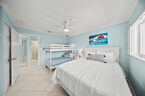 A bedroom with bunk beds, a ceiling fan, and a painting of a beach scene.