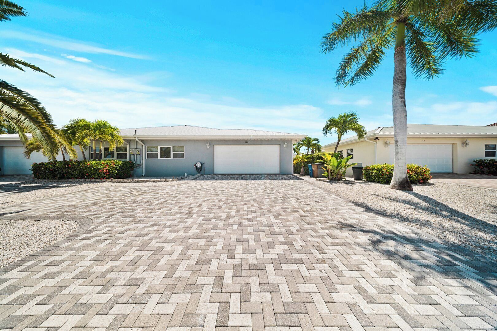 A residential property with a paved driveway, a garage, and palm trees.