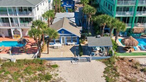 A beachfront hotel with a pool, palm trees, and beach chairs.