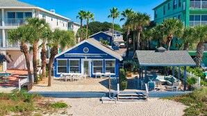 A beachfront property with a blue building, outdoor seating, and palm trees.