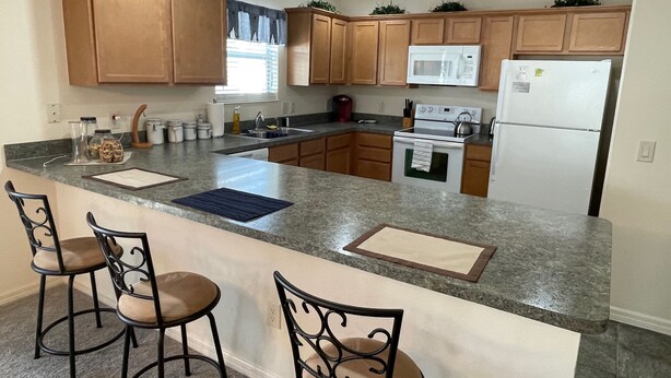 Una cocina con armarios de madera, encimera de granito, horno empotrado, refrigerador y dos taburetes de bar.