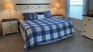 Un dormitorio con cama, dos mesitas de noche, cómoda y una ventana con cortinas.