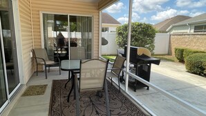 Un patio cubierto con una mesa, sillas, una parrilla y vista al jardín trasero.