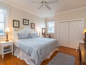 Une chambre à coucher avec un lit, des tables de chevet, un ventilateur de plafond et une porte.