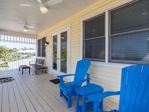 Relax on the covered porch with Adirondack chairs and a small table, surrounded by lush greenery.
