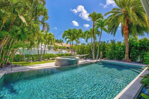 A clear blue pool surrounded by palm trees and a stone feature in the center.