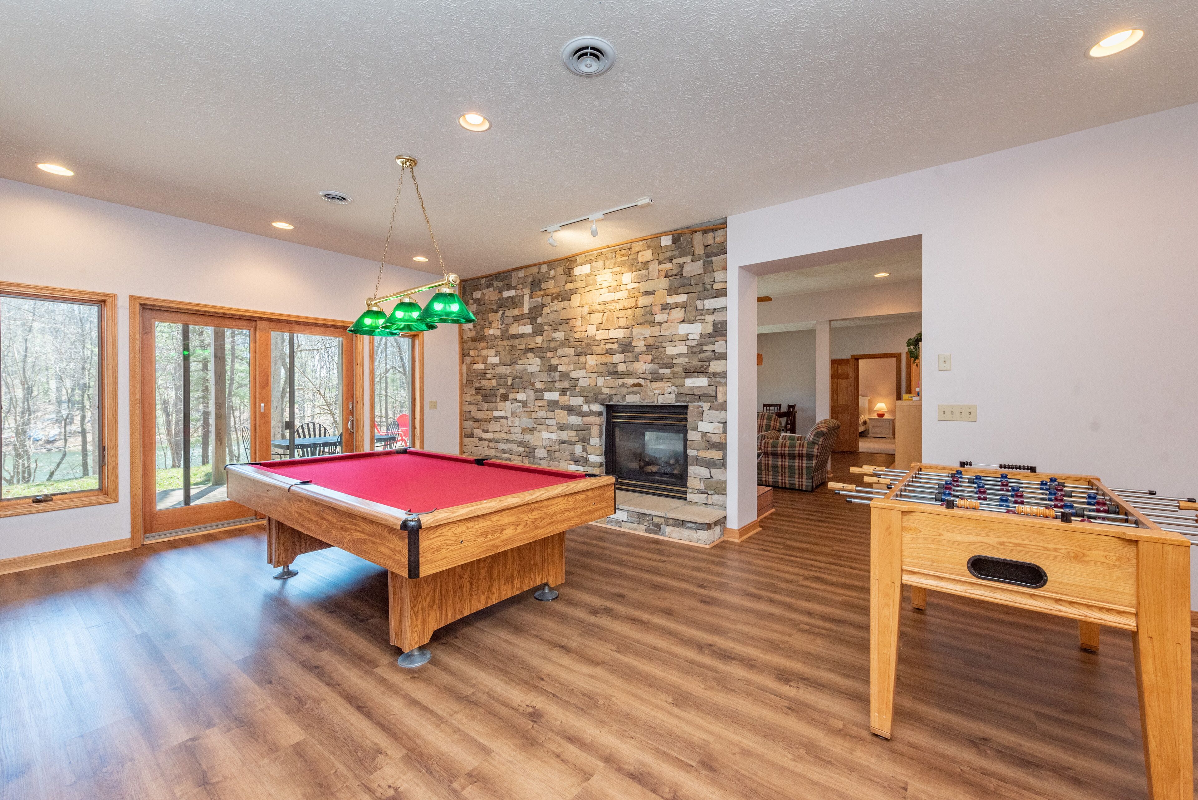 A spacious room with a pool table, foosball table, and a stone fireplace.
