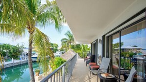 En balkon med udsigt over en lystbådehavn, palmer og en swimmingpool.