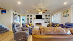 A living room with leather sofas, a fireplace, a ceiling fan, and a TV mounted above it. - A Sea Glass Estate: 9  BR, 5  BA House in Crystal Beach, Sleeps 34 (Bolivar Peninsula)