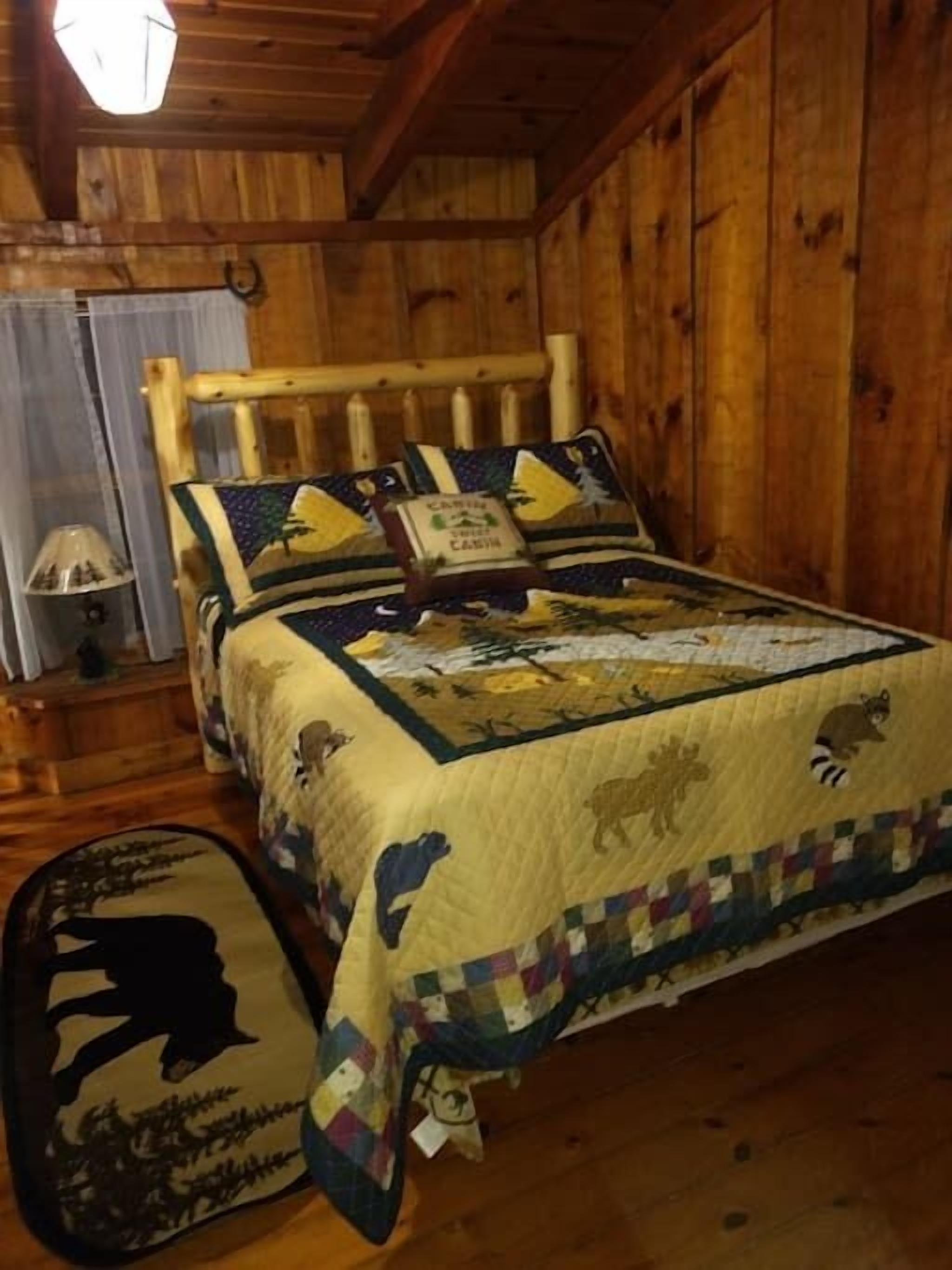A wooden cabin bedroom with a bed featuring a quilt with animal prints, a wooden headboard, and a small bedside table with a lamp.