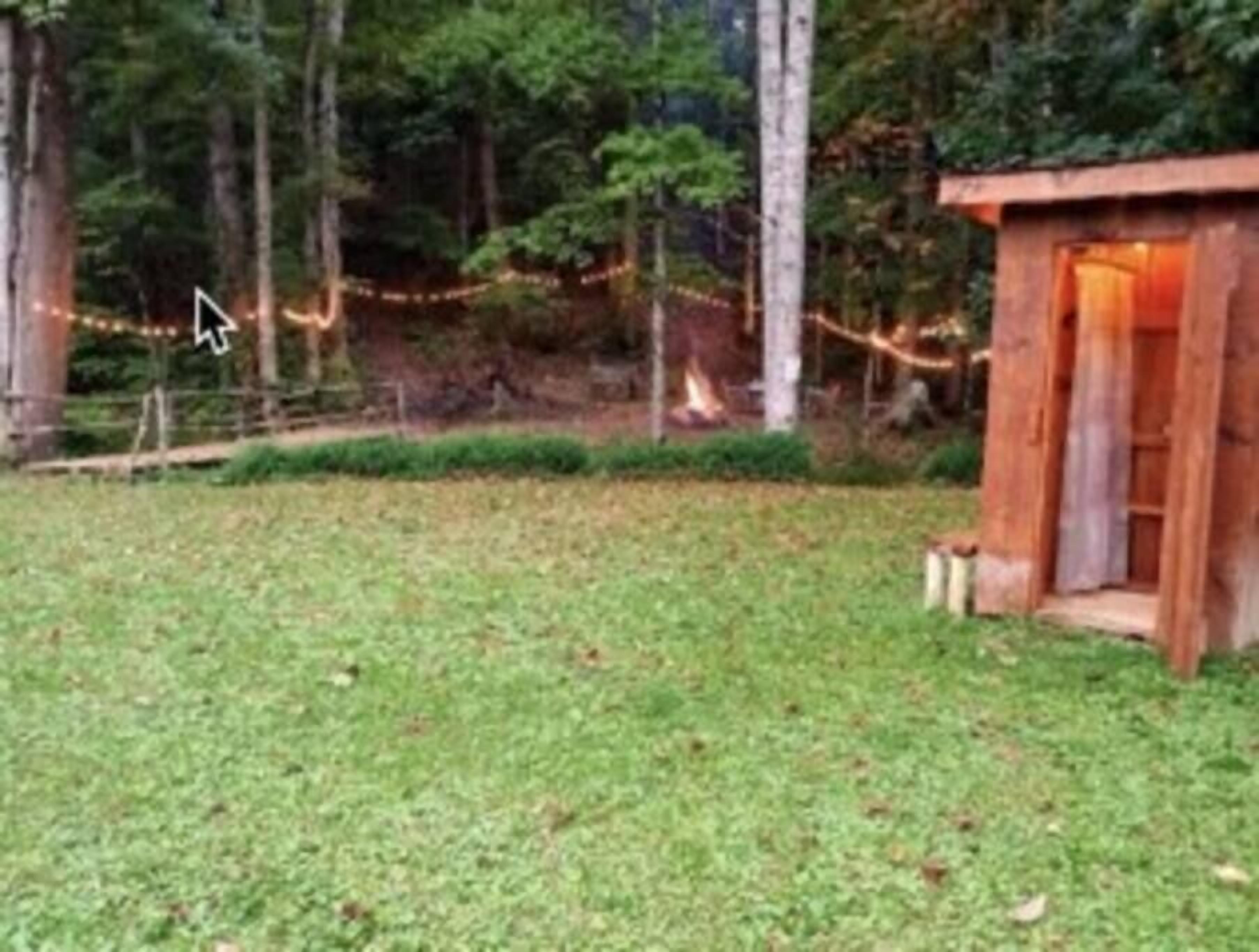 A rustic wooden cabin with a small porch, surrounded by a grassy yard and trees.