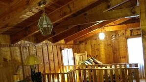 A cabin with a wooden interior, a bed with a bear design, a lamp, and a window.