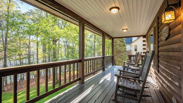 A wooden deck with rocking chairs overlooking a forested area and a lake. - Enjoy Adventure & Relaxation w/ Hot Tub & Fire Pit (McHenry)