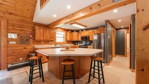 A kitchen with wooden cabinets, a central island with stools, stainless steel appliances, and a ceiling with exposed beams. - Enjoy Adventure & Relaxation w/ Hot Tub & Fire Pit (McHenry)