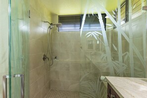 Une douche fermée par des parois en verre, dotée d’un pommeau de douche à main et d’un robinet mural.