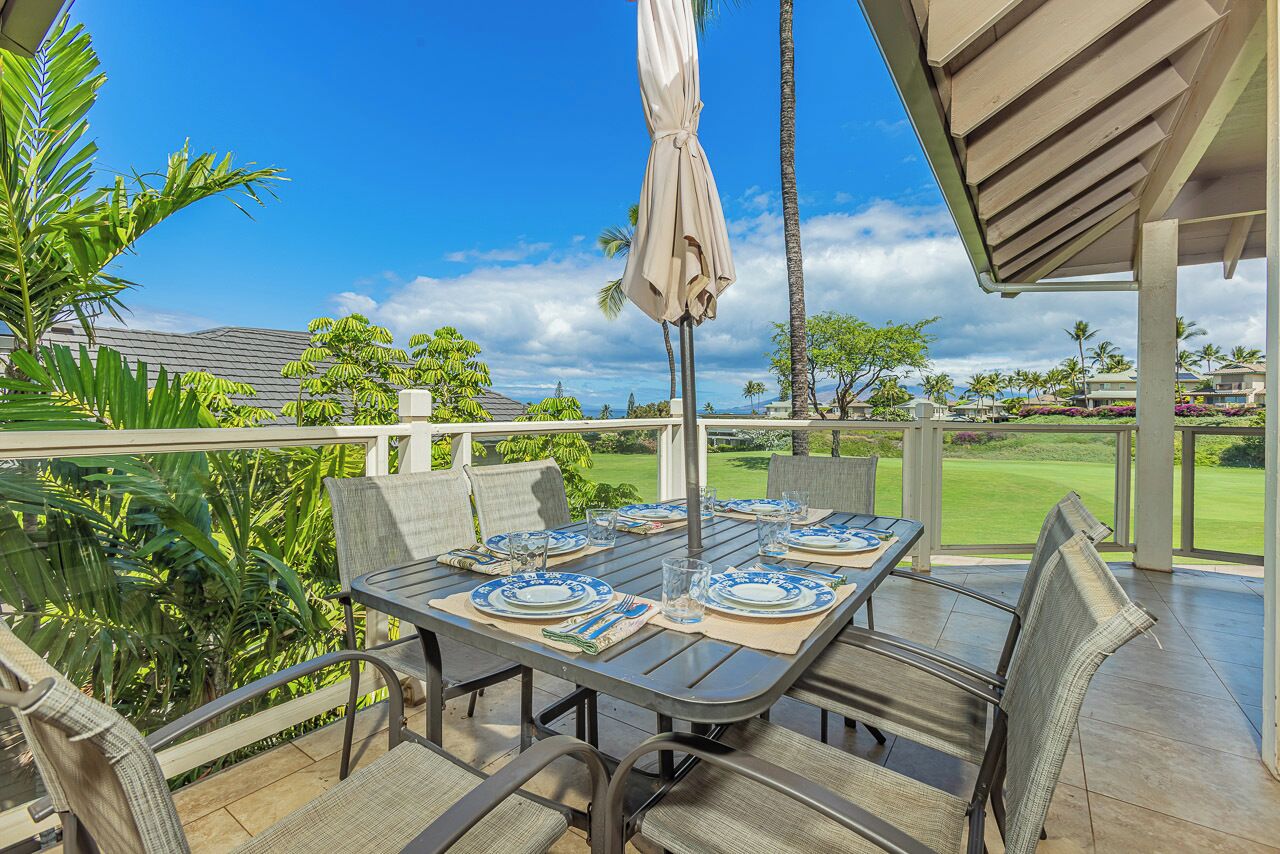 An outdoor dining area with a table set for four, surrounded by chairs, and a covered umbrella.