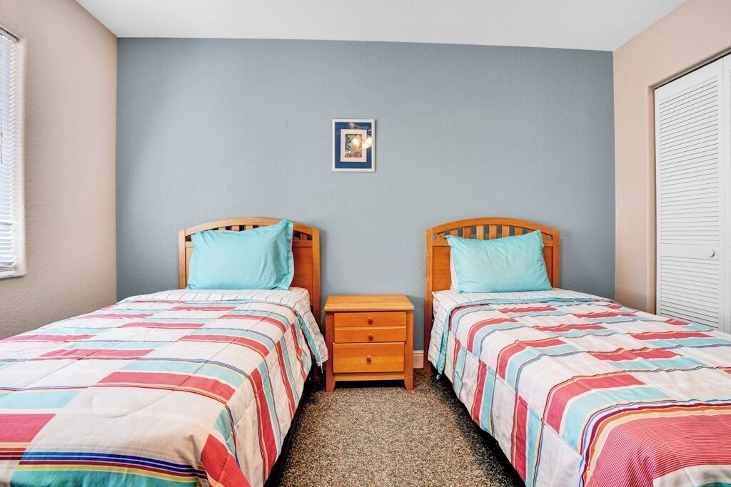 A bedroom with two single beds, a small wooden nightstand, and a framed picture on the wall.