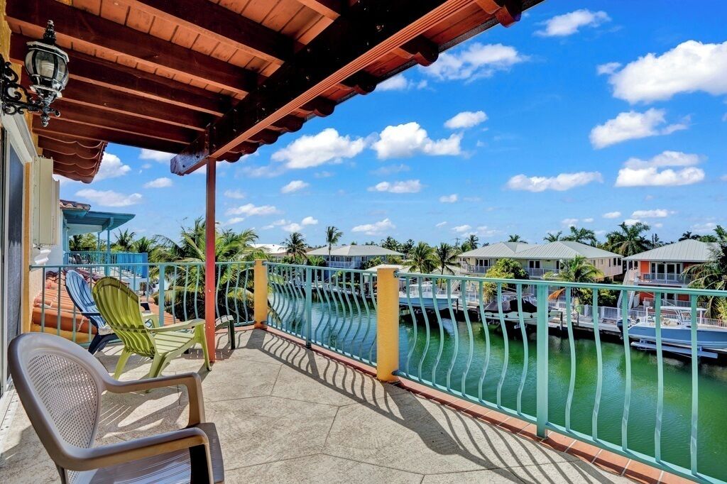 A balcony with a view of a marina, a covered area with chairs, and a railing.